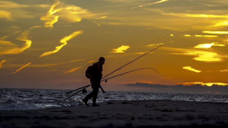 A man leaves the beach at sunset after surf fishing...