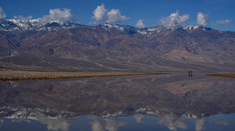 Snow capped mountains are reflected in water at Badwater Basin,...