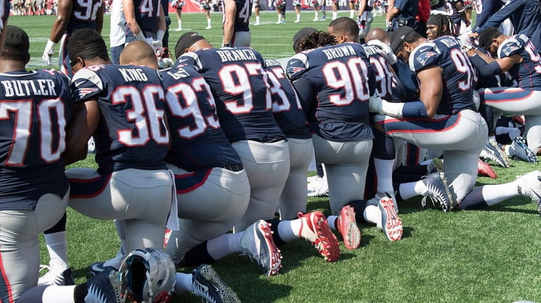 Patriots players hold hands and kneel during the national anthem...
