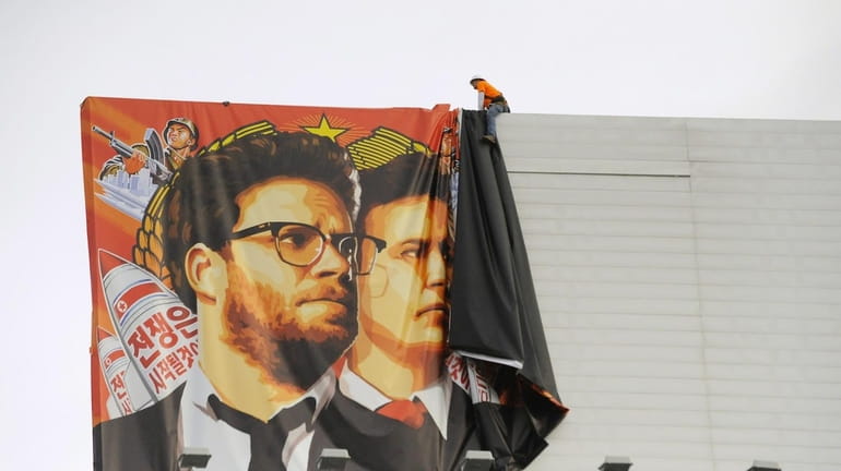 Workers remove a poster banner for "The Interview" from a...