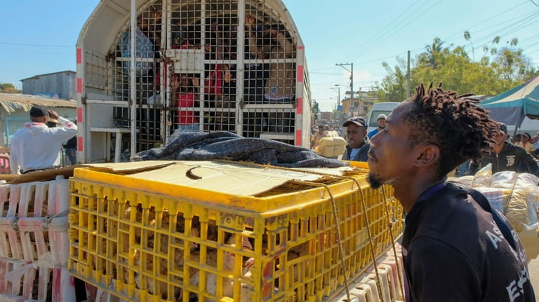 A vendor pushes crates of chickens past a police truck...