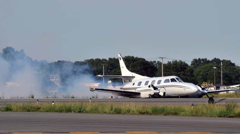 A twin-engine airplane smokes seconds after making a belly-landing on...