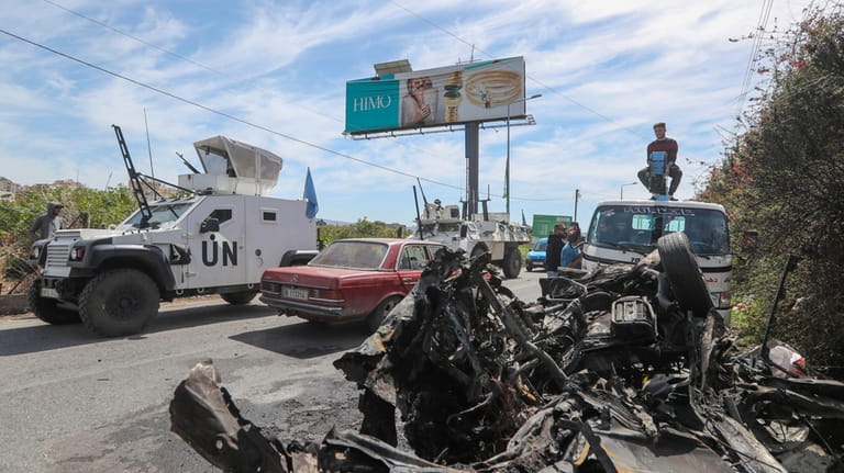 A U.N peacekeeper vehicle passes next of a destroyed car...