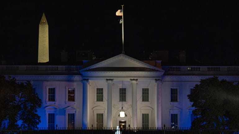 The White House is lit in blue and white, the...