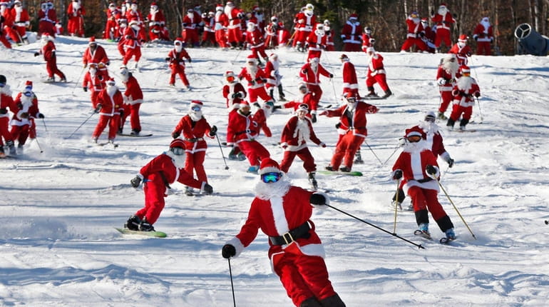Skiers and snowboarders dressed as Santa take a run en...