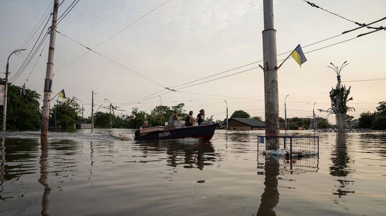 People ride by a boat through a flooded neighborhood in...