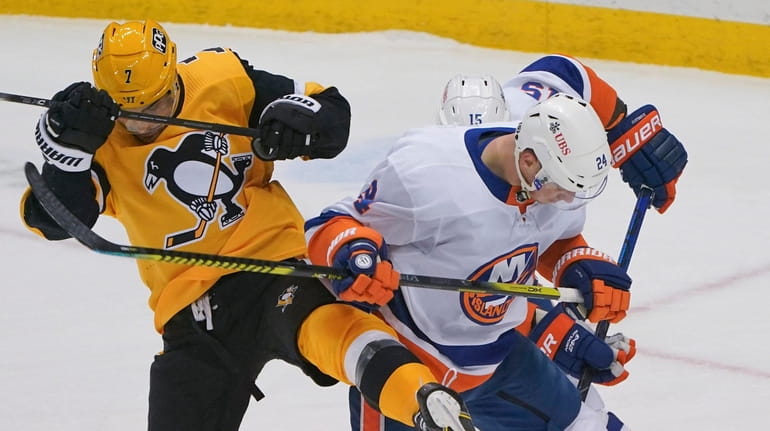 The puck slides under the Penguins' Colton Sceviour and the Islanders'...