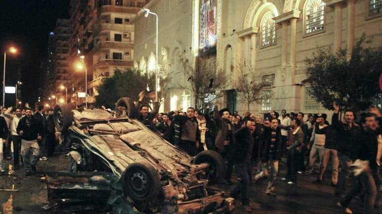 Worshippers shout around an exploded car in front of a...