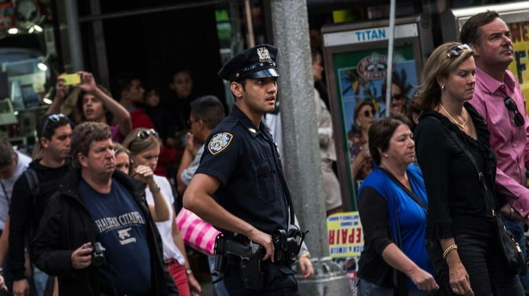 An NYPD officer walks with a crowd in Times Square....