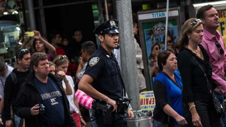 An NYPD officer walks with a crowd in Times Square....
