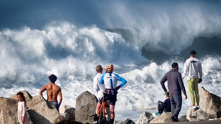 Beachgoers watch as turbulent surf pounds the coast at Manhattan...