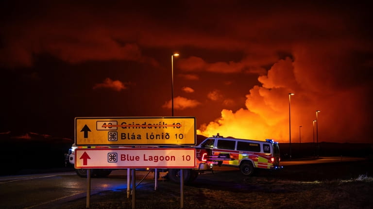 Emergency vehicles are stationed on a road leading to volcanic...