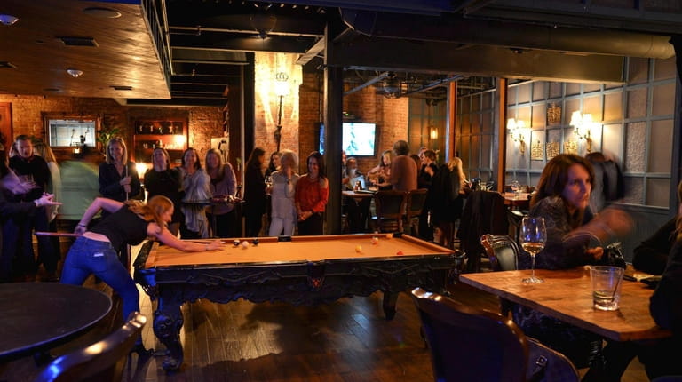 Patrons chat, sip drinks and play billiards inside of the...