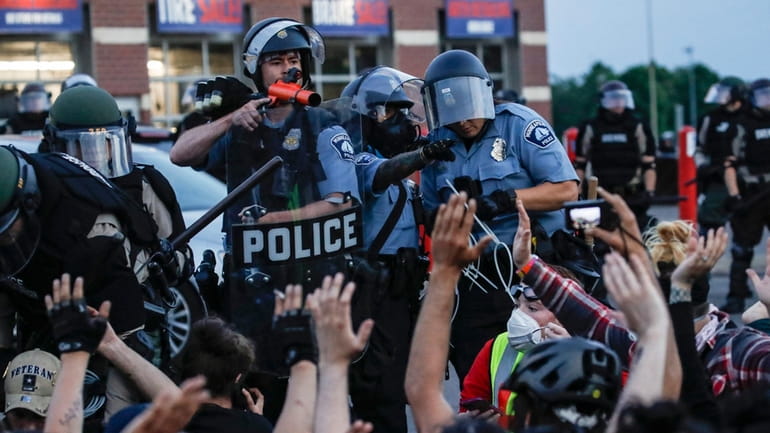 A police officer points a hand cannon at protesters who...