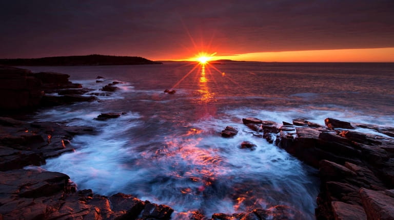 The sun's rays strike the rocky coast of Acadia National...