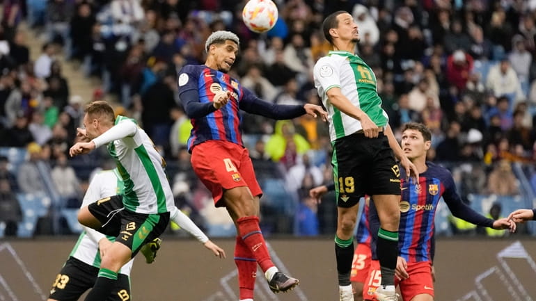 Barcelona's Ronald Araujo, lef, and Betis' Luiz Felipe jump for...
