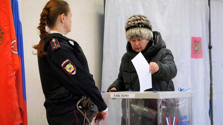 A woman casts a ballot as a police officer guards...