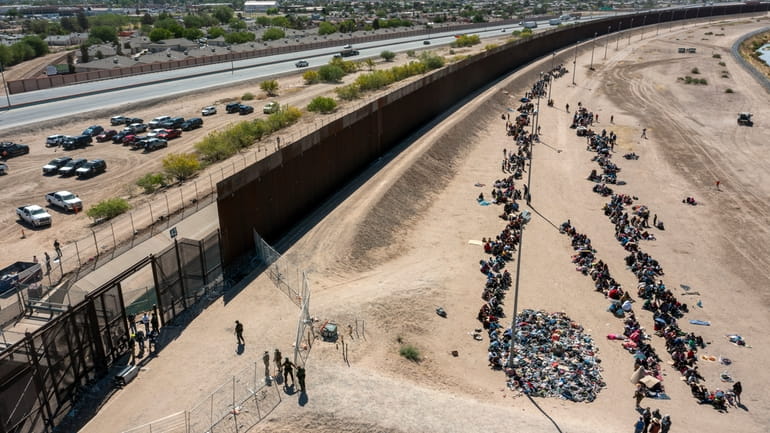 Migrants form lines outside the border fence waiting for transportation...