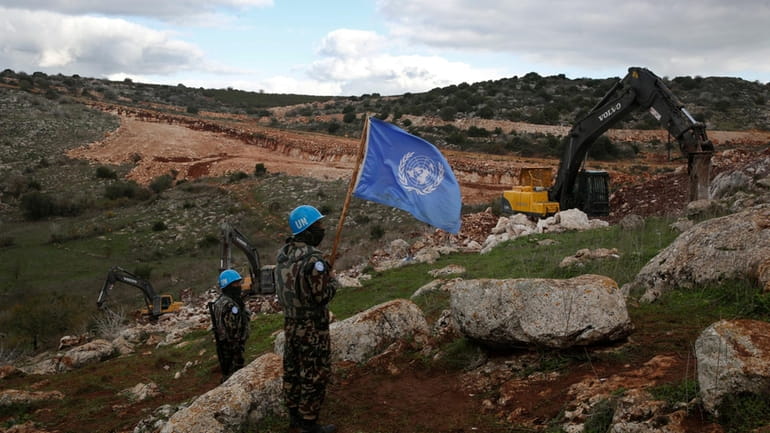 UN peacekeepers hold their flag, as they observe Israeli excavators...