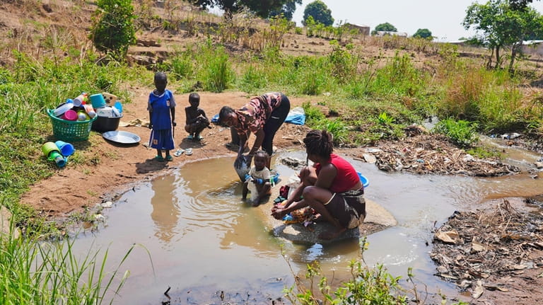 Women wash clothes and dishes in a stream in Bouar,...