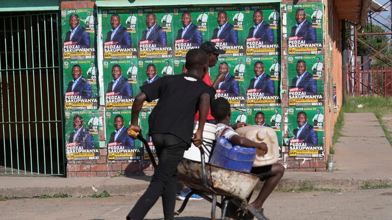 A young boy pushes a wheelbarrow past campaign posters in...