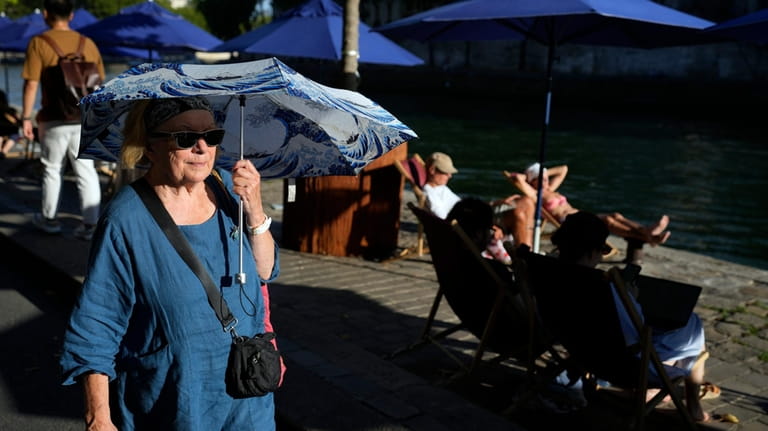 A woman shelters from the sun with an umbrella along...