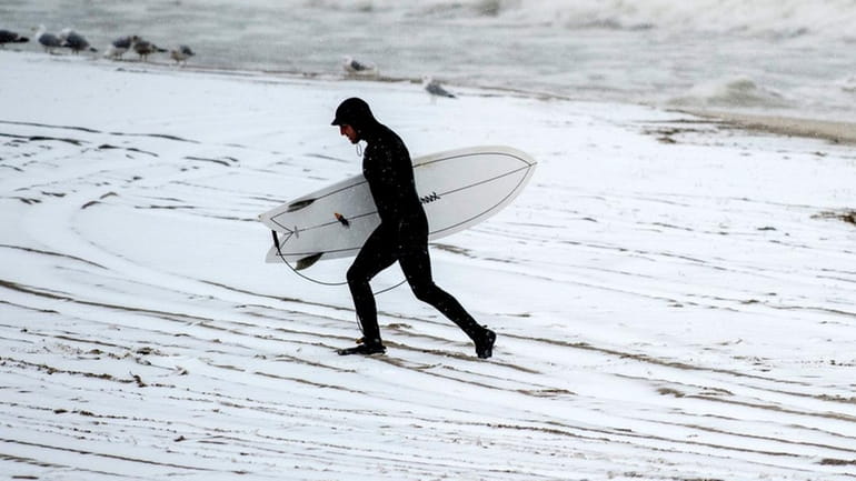 A surfer in Long Beachleaves the snowy beach on the first...