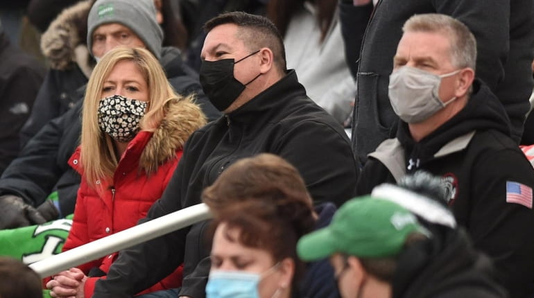 Spectators wear masks in the stands at a football game between Farmingdale...