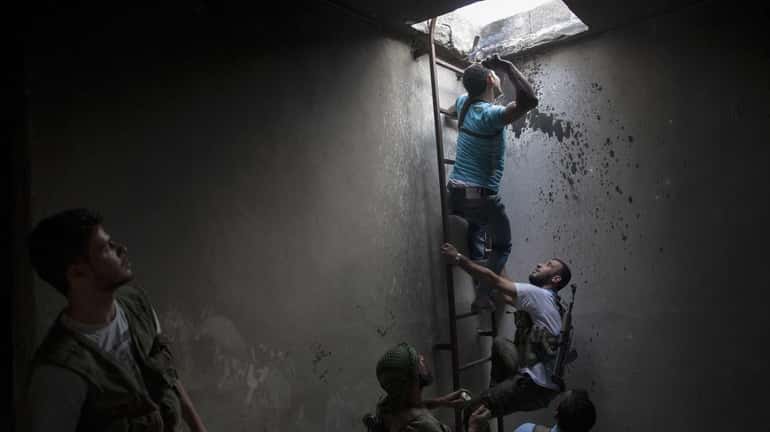 Syrian rebels observe as a comrade prepares to throw a...