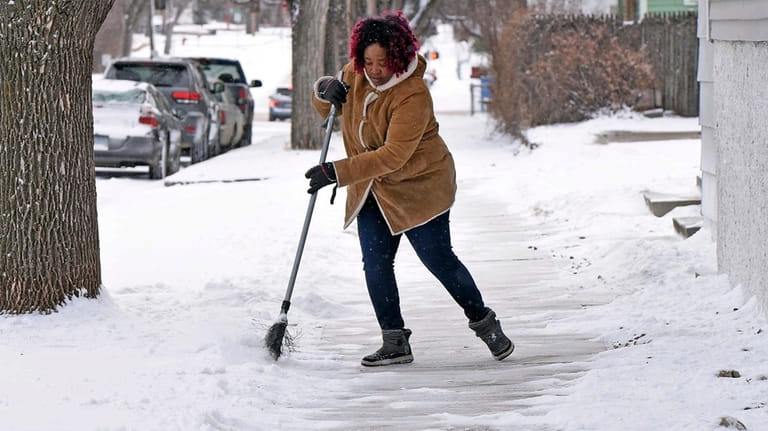 Josephine Wiea sweeps the sidewalk of snow at the International...