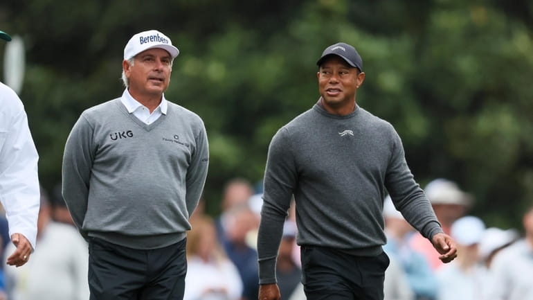 Fred Couples, left, and Tiger Woods talk as they walk...