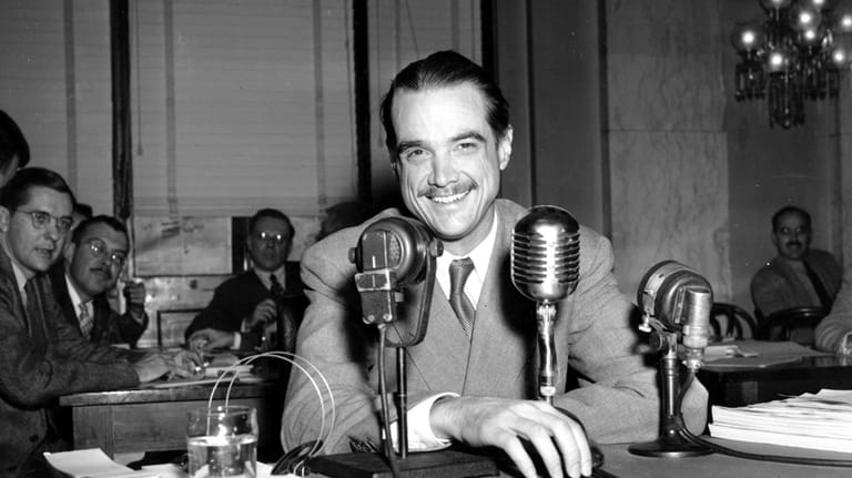Howard Hughes smiles as he sits in the witness chair...