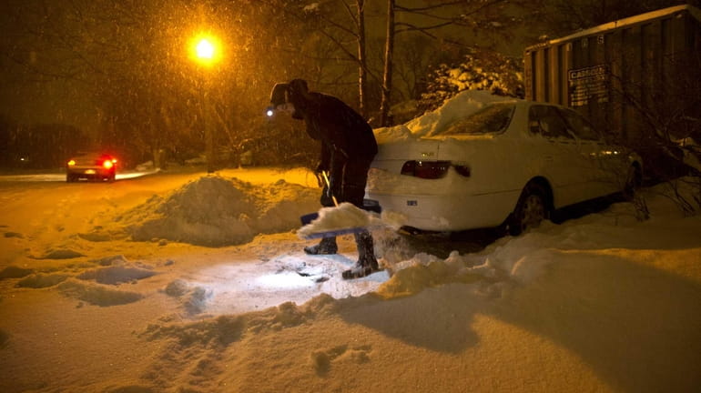 Katharine Lynch uses a head lamp and snow shovel to...