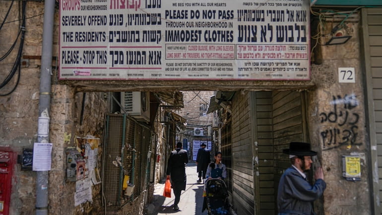 Ultra-Orthodox Jews walk past a sign calling on women to...