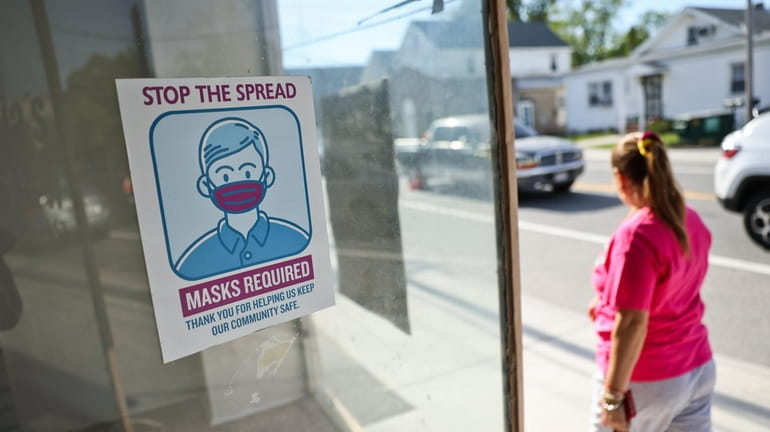 A person passes a storefront with a posted mask sign...