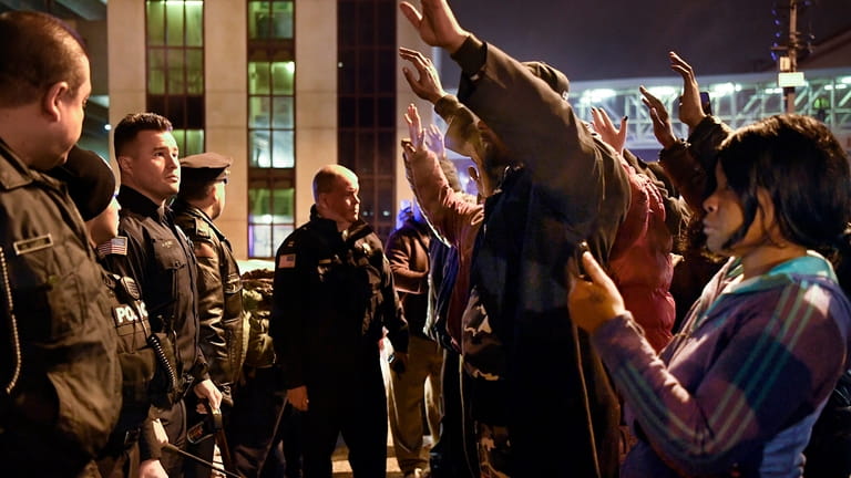 Protesters raise their hands as they face police officers during...