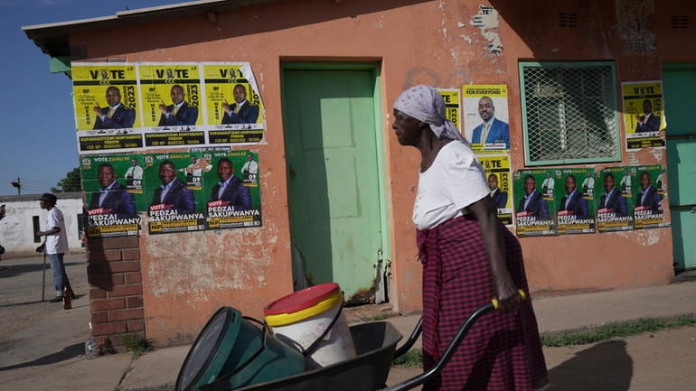An elderly woman pushes a wheelbarrow past campaign posters in...