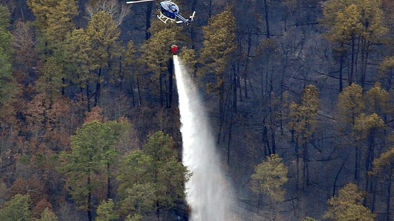 A state police helicopter drops water over hot spots in...