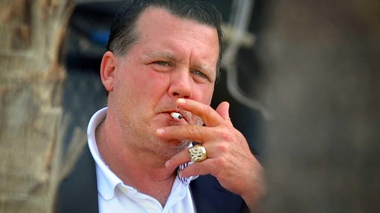 New York Yankees owner Hank Steinbrenner smokes a cigarette outside...
