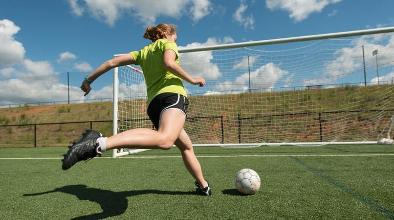 A soccer player practices shots on a turf field.