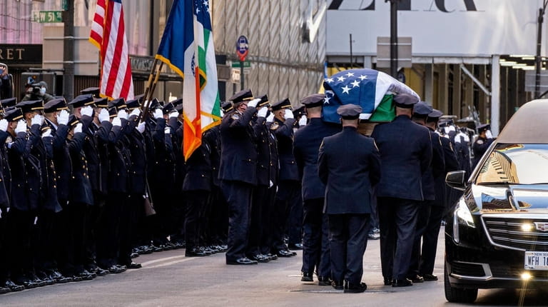 NYPD officers from the 32nd Precinct salute as the body...