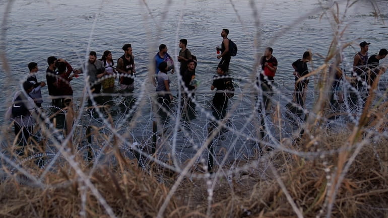 Migrants wait to climb over concertina wire after they crossed...