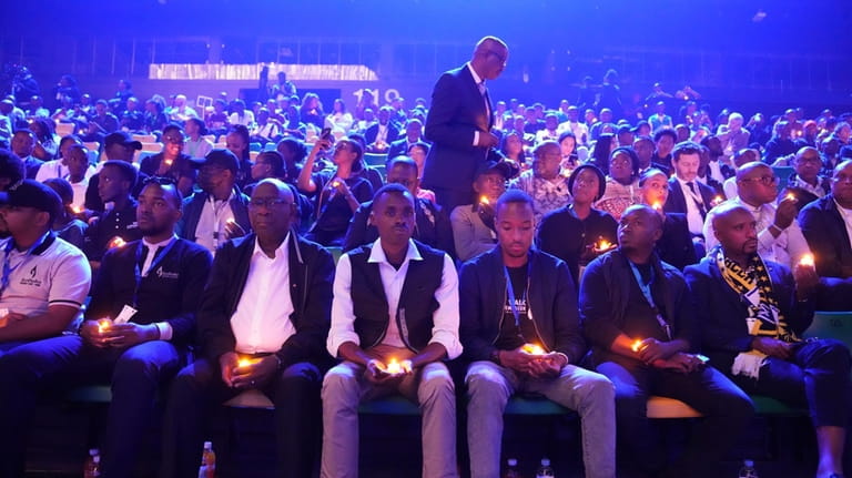 Rwandans and others sitting in the stands, hold candles as...