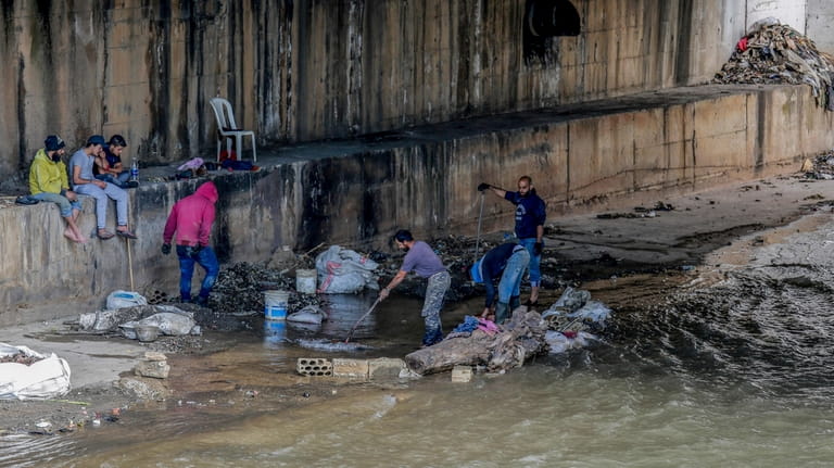 Men sifts through a sewer for valuables along the foreshore...