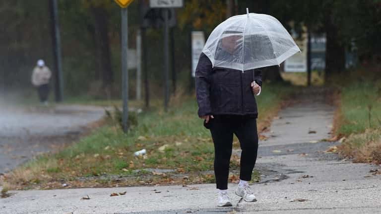 A woman shields herself from rain as she walks along...