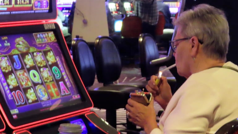 A gambler lights a cigarette at a slot machine in...