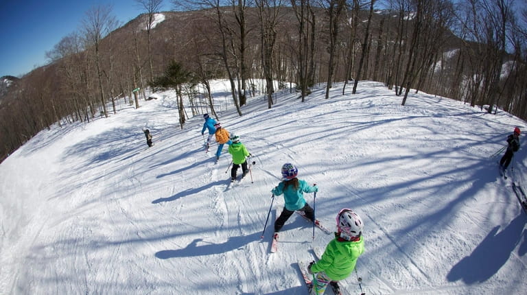 A teacher leads a group of ski schoolers down the...
