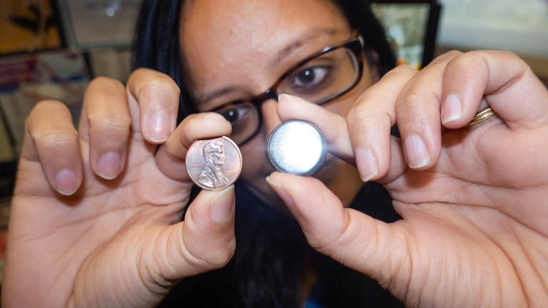 Dr. Neha Patel shows a penny and a similar-sized button battery....