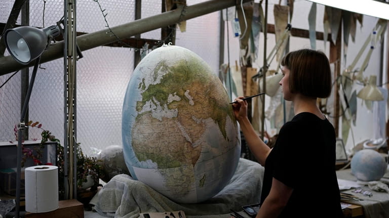 An artist paints a globe at a studio in London,...