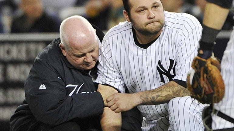 A trainer, left, helps Yankees relief pitcher Joba Chamberlain, who...
